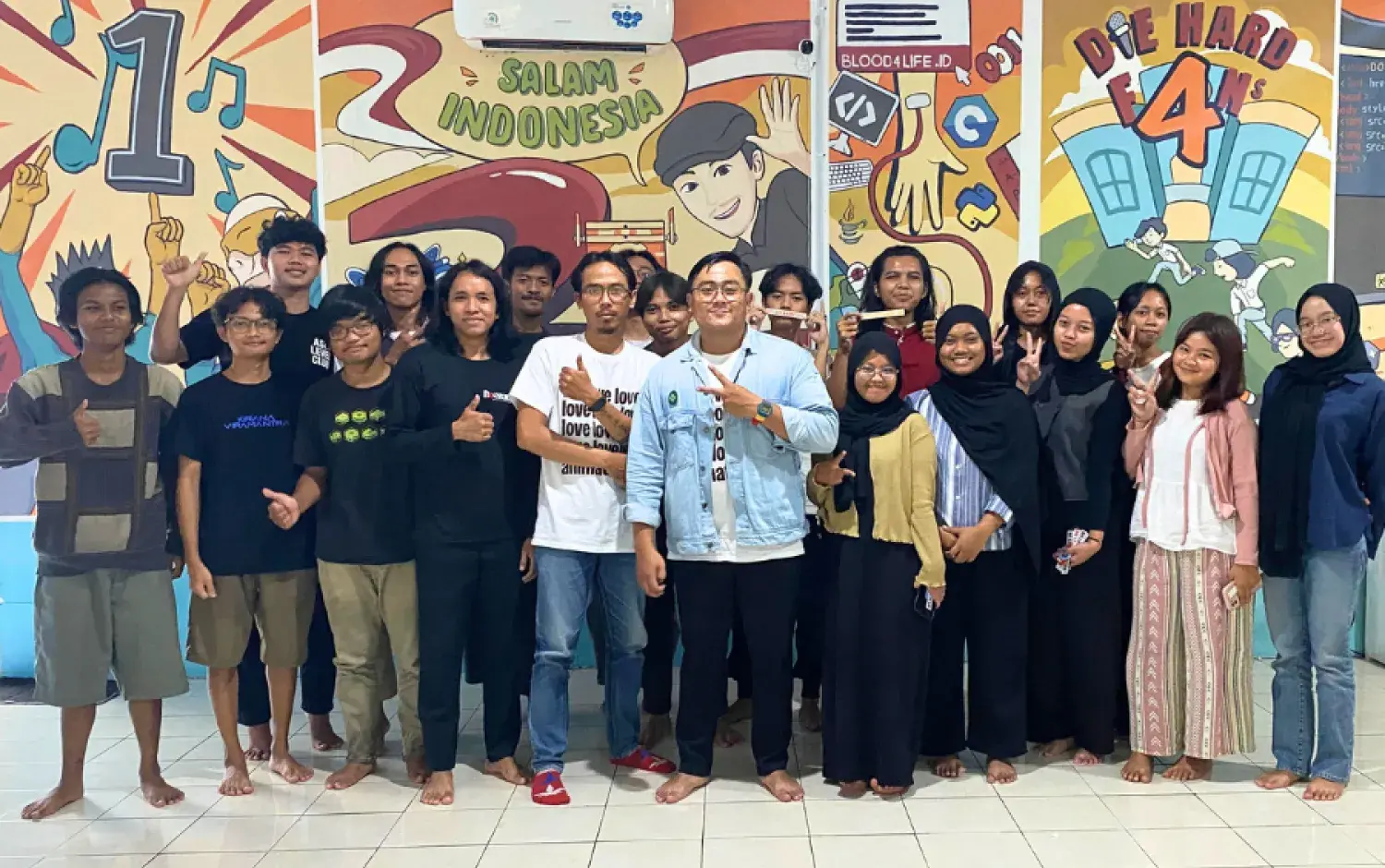 Large group posing indoors in front of colorful mural wall with illustrated graphics and text.