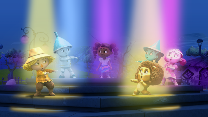 Dee and her friends performing on a stage with brightly colored lights beaming down on them
