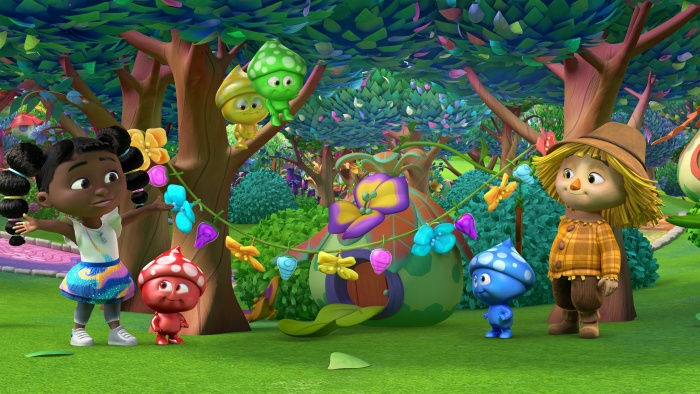 Dee and her friends in a woodland area with bright colored flowers hanging between the trees