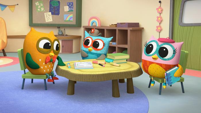 Three colorful owlets sitting at a round table with art supplies.