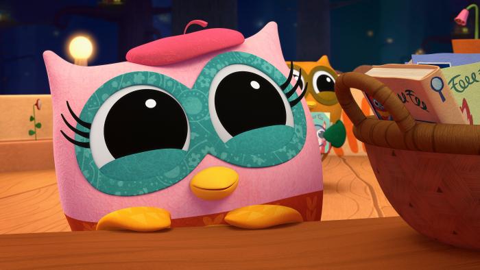 Pink owl peeking up from a counter smiling.