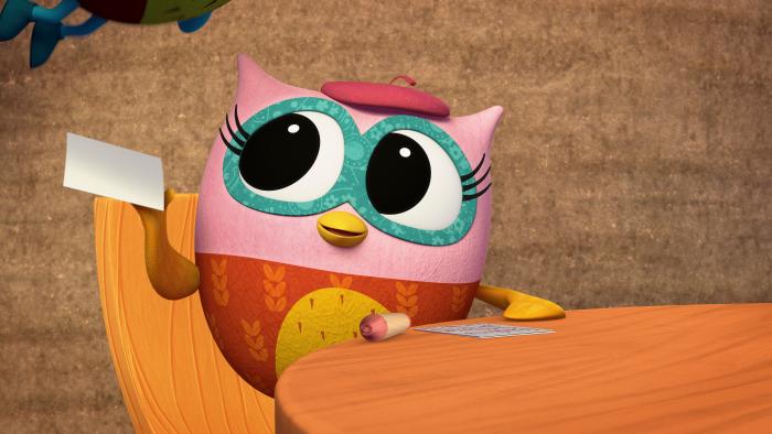 Pink owl sitting a table with a piece of paper in her outstretched wing and a slightly questioning look.